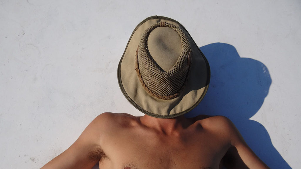顔に帽子をかぶりビーチに寝転ぶ男性